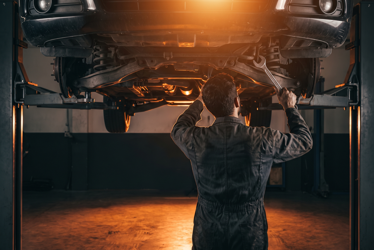 Mechanic under a car raised on a two post hoist, working with a spanner